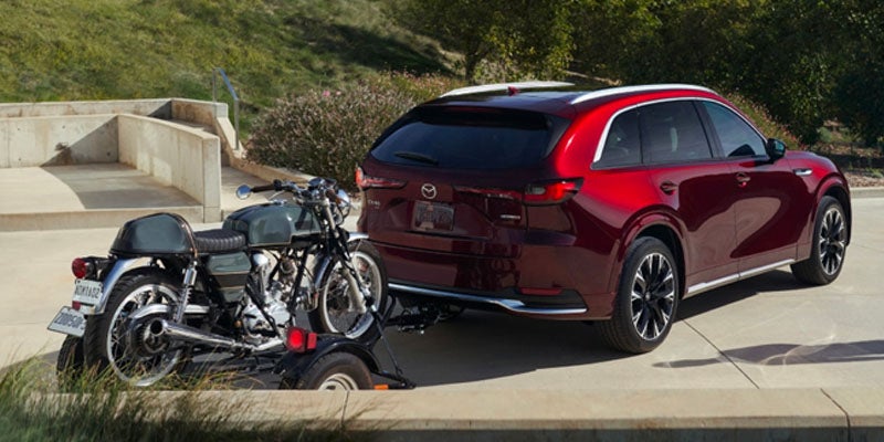 A 2025 Mazda CX-70 carrying a small trailer with a motorcycle on it