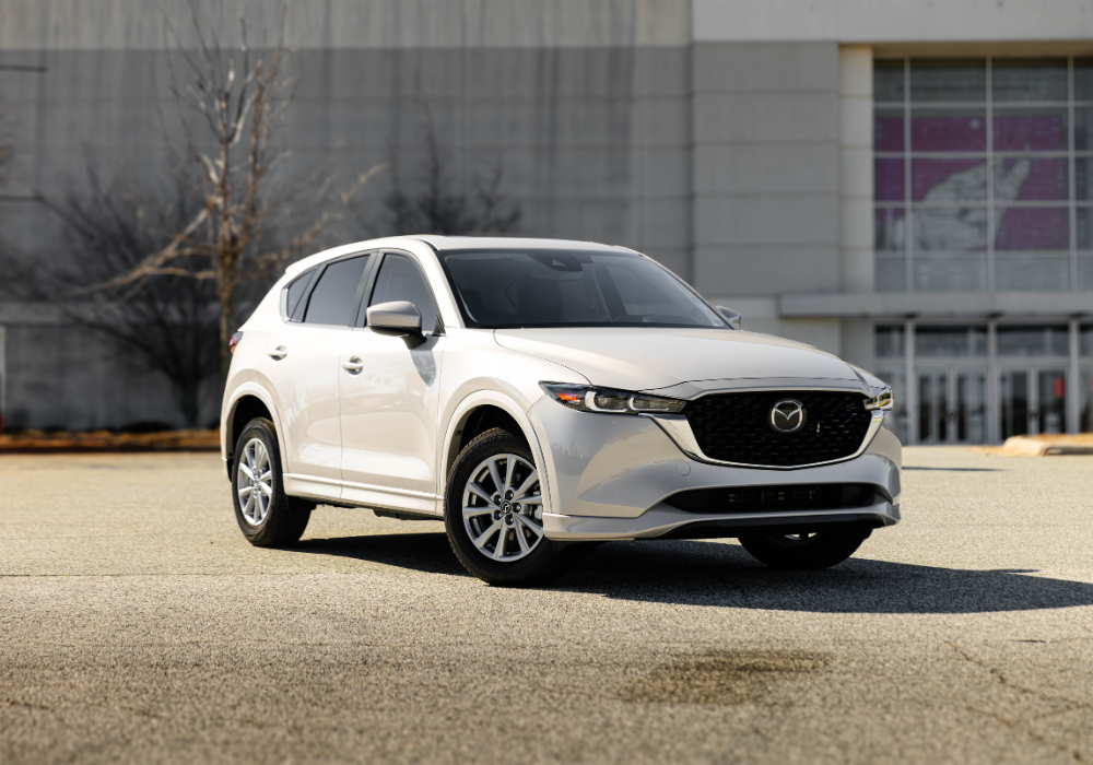 White 2025 Mazda CX-5 parked in front of a large building.