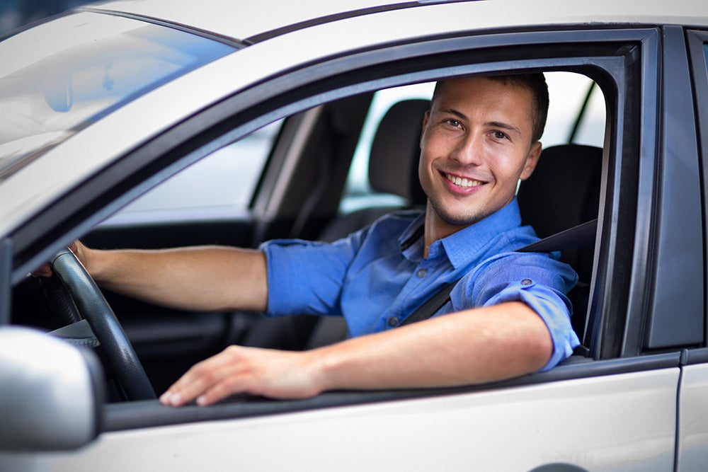 A male in the driver's seat of a car smiling
